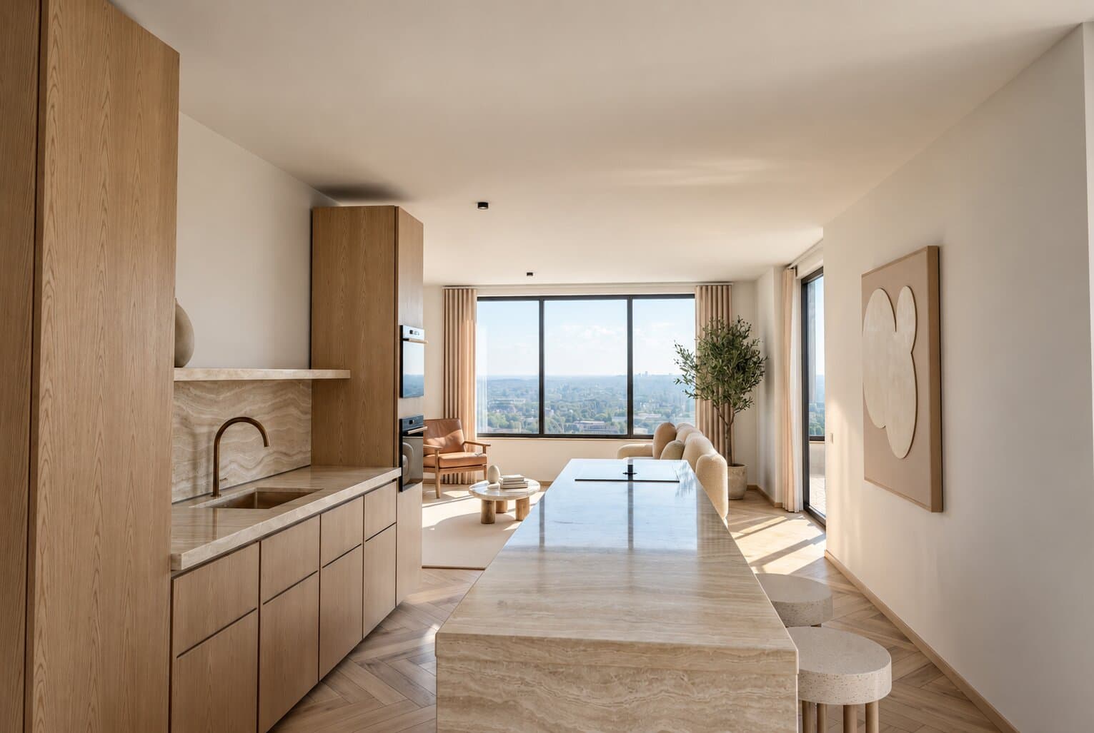 Artist impression of a kitchen with oak cupboards, a travertine worktop and a long travertine island with two stools, looking through to a living room with a leather armchair, an olive tree and a wide window over the city and the green beyond.